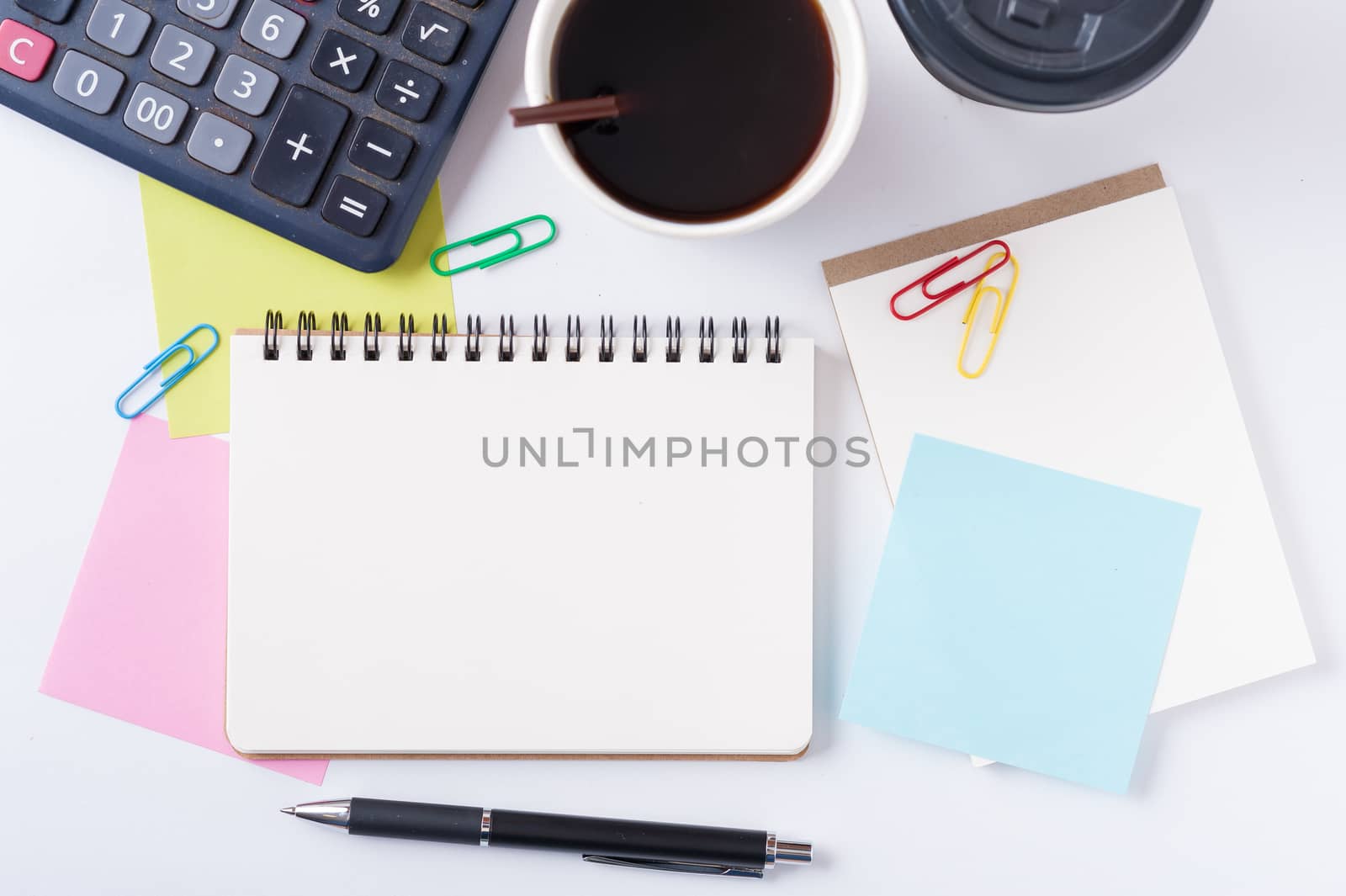 Opened notebook with blank space for text or message, sticky paper, calculator, and take away coffee cup on office table