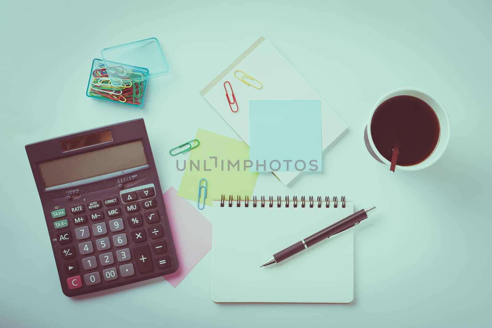 Opened notebook with blank space for text or message, sticky paper, calculator, and take away coffee cup on office table with vintage filter effect