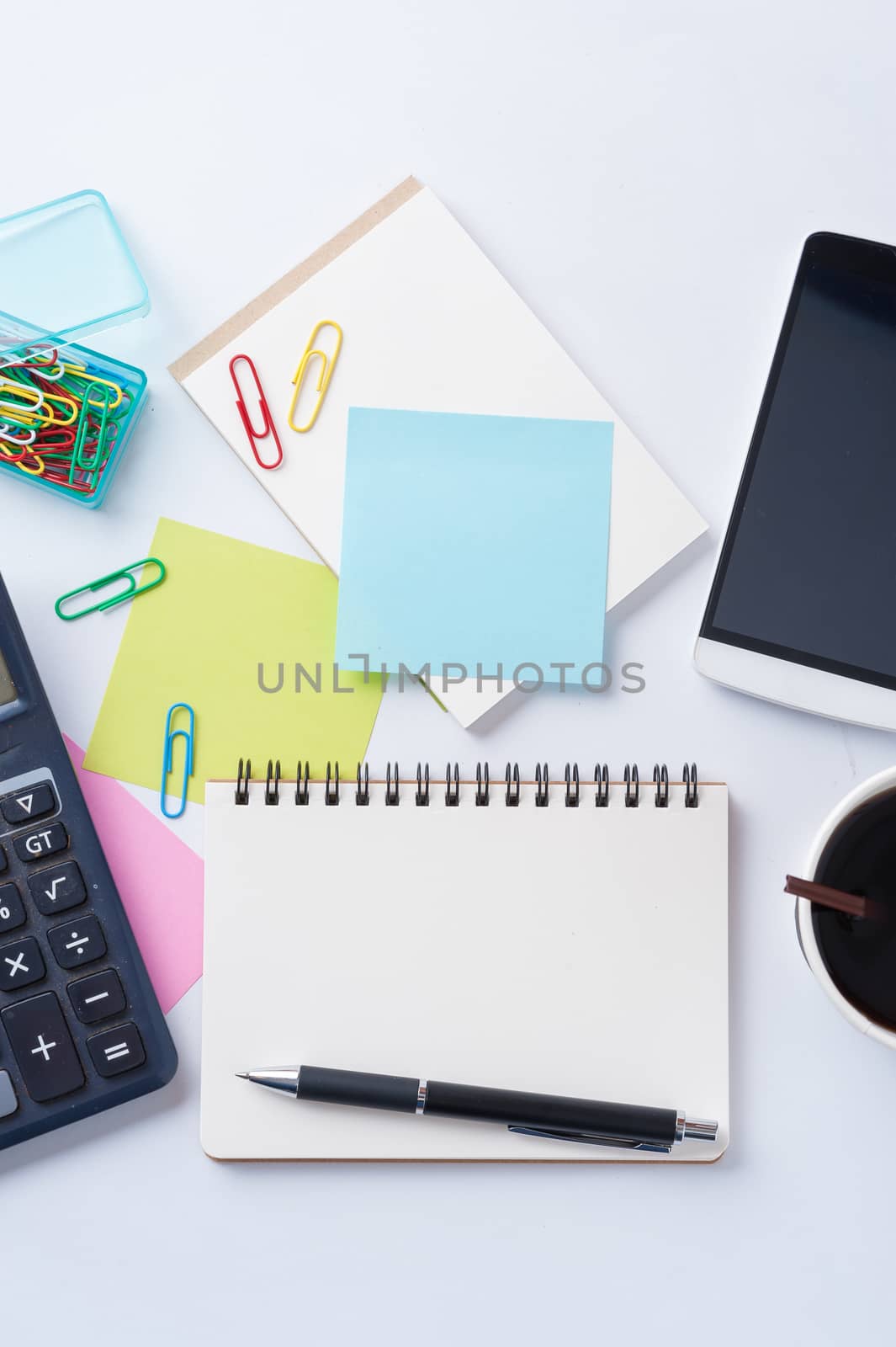 Opened notebook with blank space for text or message, sticky paper, calculator, smart phone, and take away coffee cup on office table