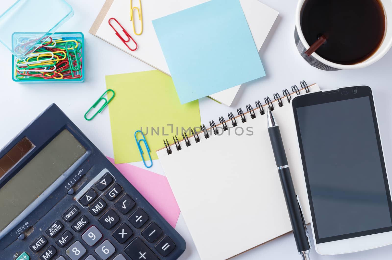 Opened notebook with blank space for text or message, sticky paper, calculator, smart phone, and take away coffee cup on office table