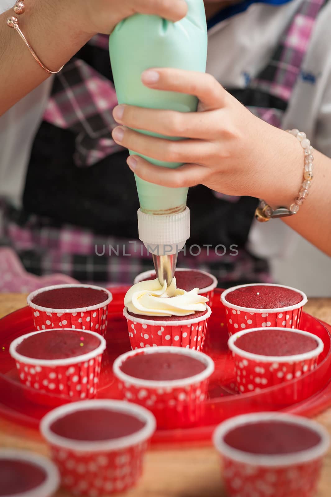 The action of making red velvet cupcakes. Woman hand piping cream cheese on cupcake.