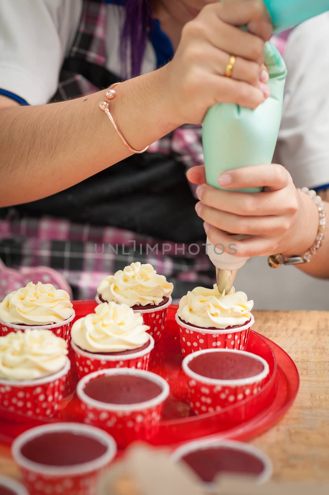 The action of making red velvet cupcakes. Woman hand piping cream cheese on cupcake.