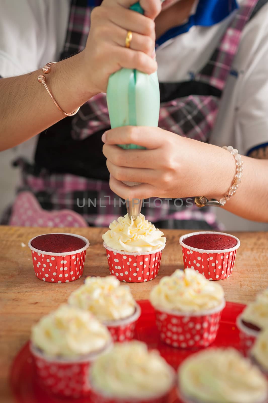 The action of making red velvet cupcakes. Woman hand piping cream cheese on cupcake.