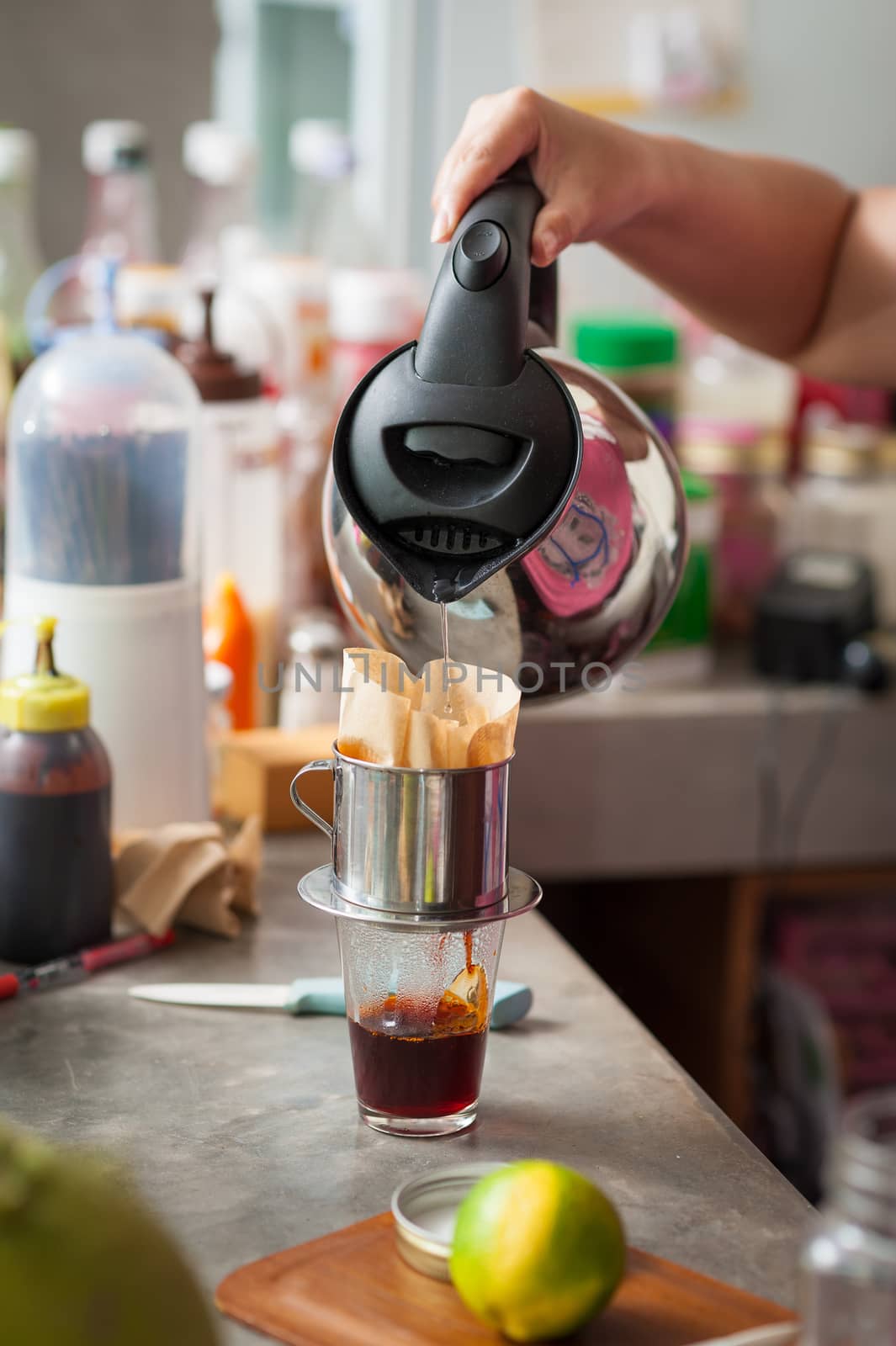 The process of making Thai lemon tea. Woman right hand pouring hot water into dripper above tea glass