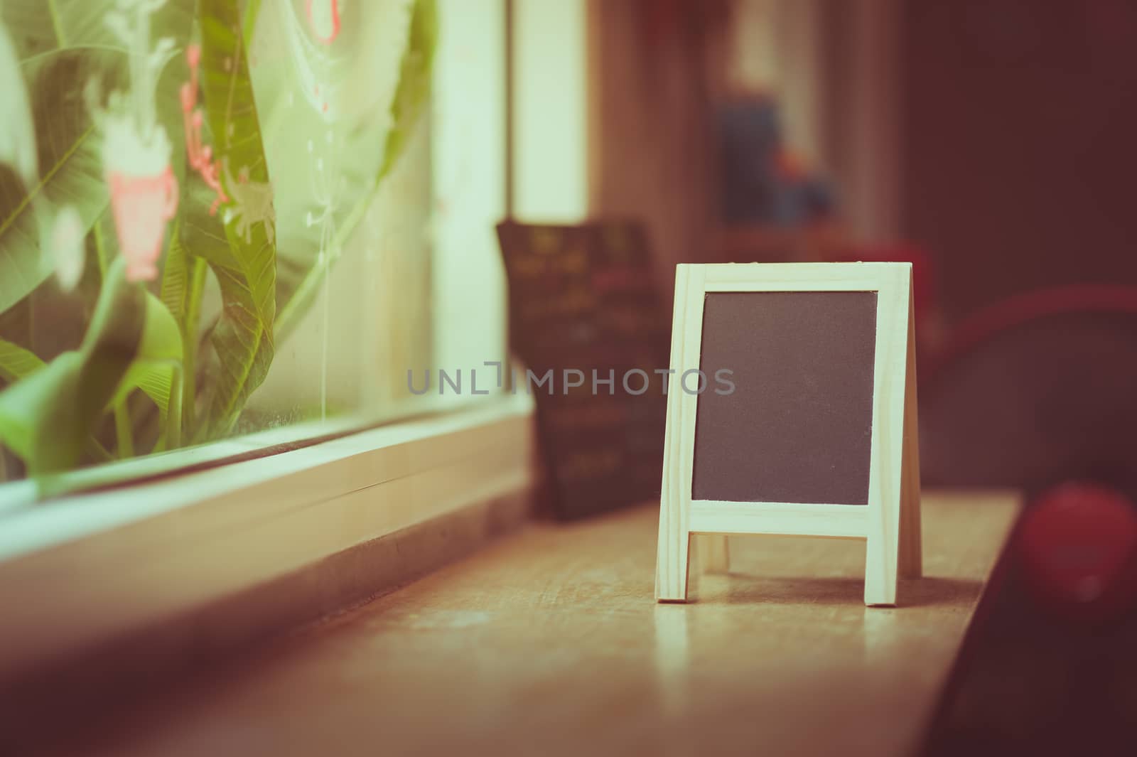 Small A-frame black board with blank area for text or message on wood bar in cafe wih vintage filter effect