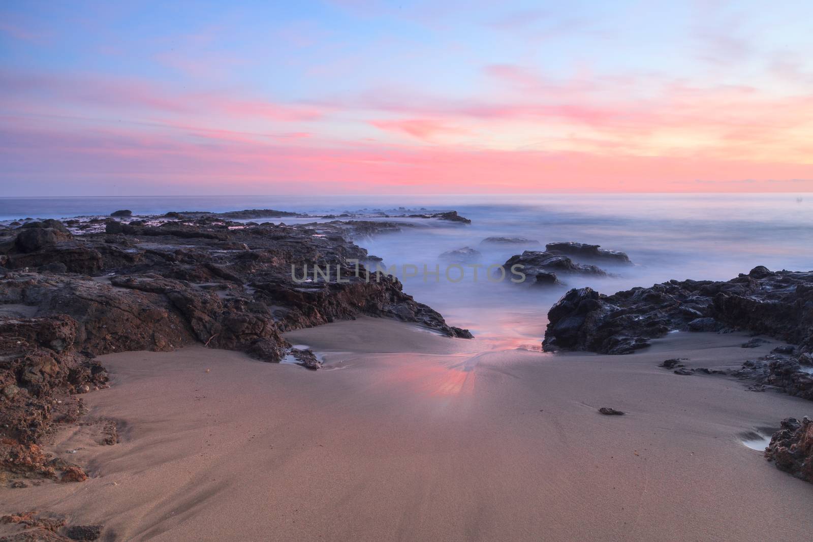 Long exposure of sunset over rocks, giving a mist like effect over ocean in Laguna Beach, California, United States