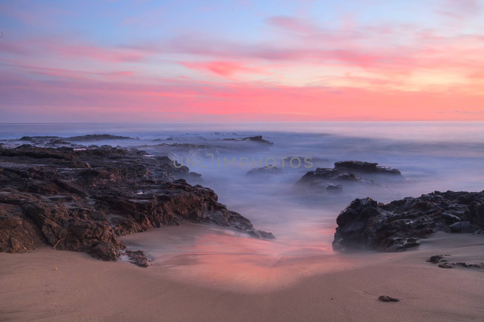 Long exposure of sunset over rocks, giving a mist like effect over ocean in Laguna Beach, California, United States