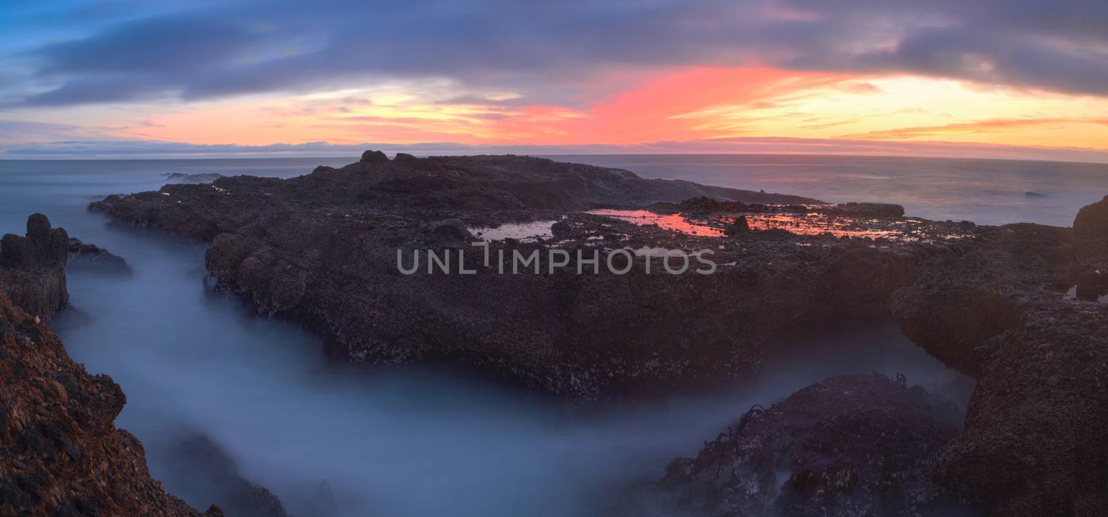 Long exposure of sunset over rocks, giving a mist like effect over ocean in Laguna Beach, California, United States