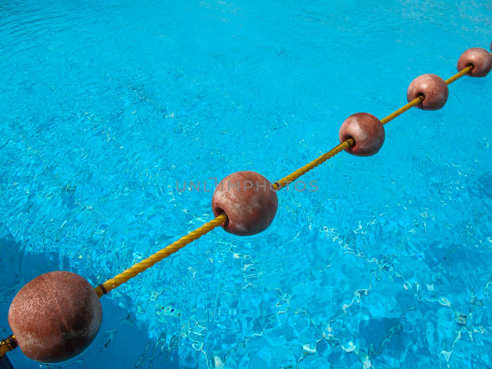 Diagonal line of the buoys on the rope, dividing the swimming pool. Fresh bright blue color of the water with small waves in the windy weather.