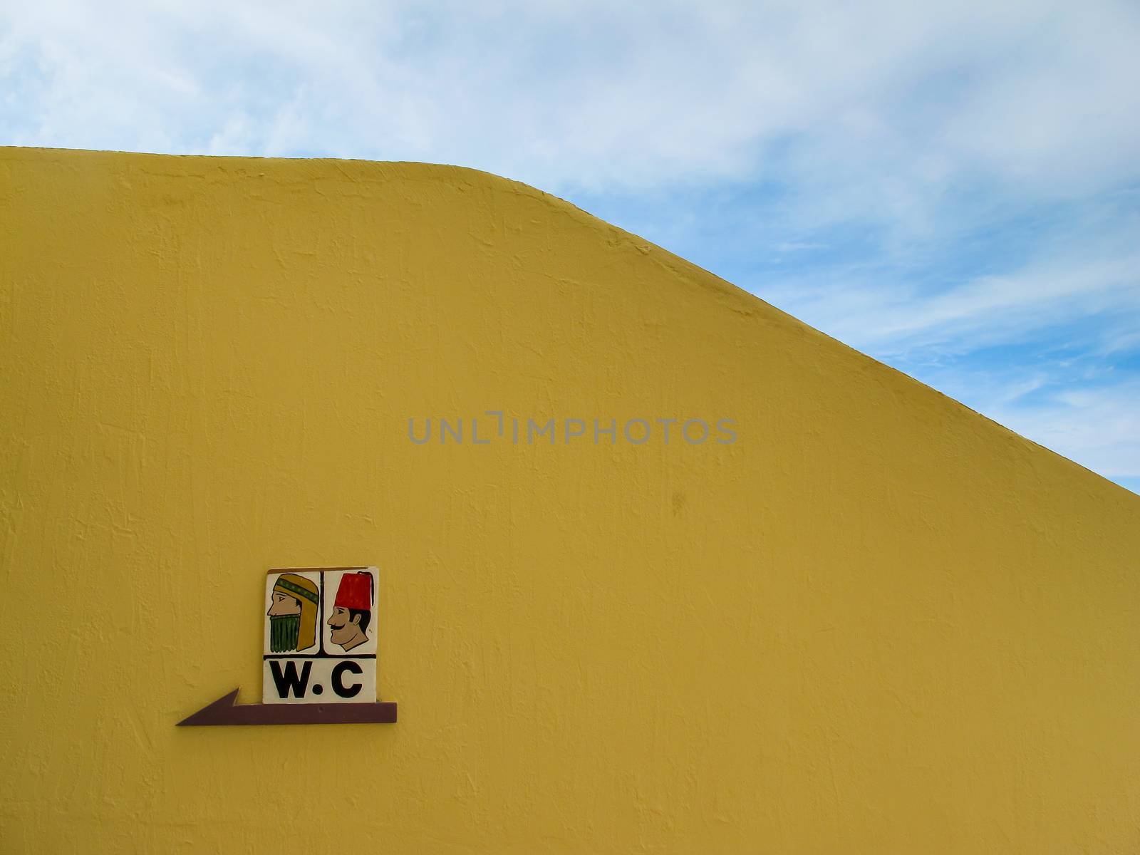 Yellow painted fence outdoors with a WC sign. Traditionally dressed man and woman. Egypt.