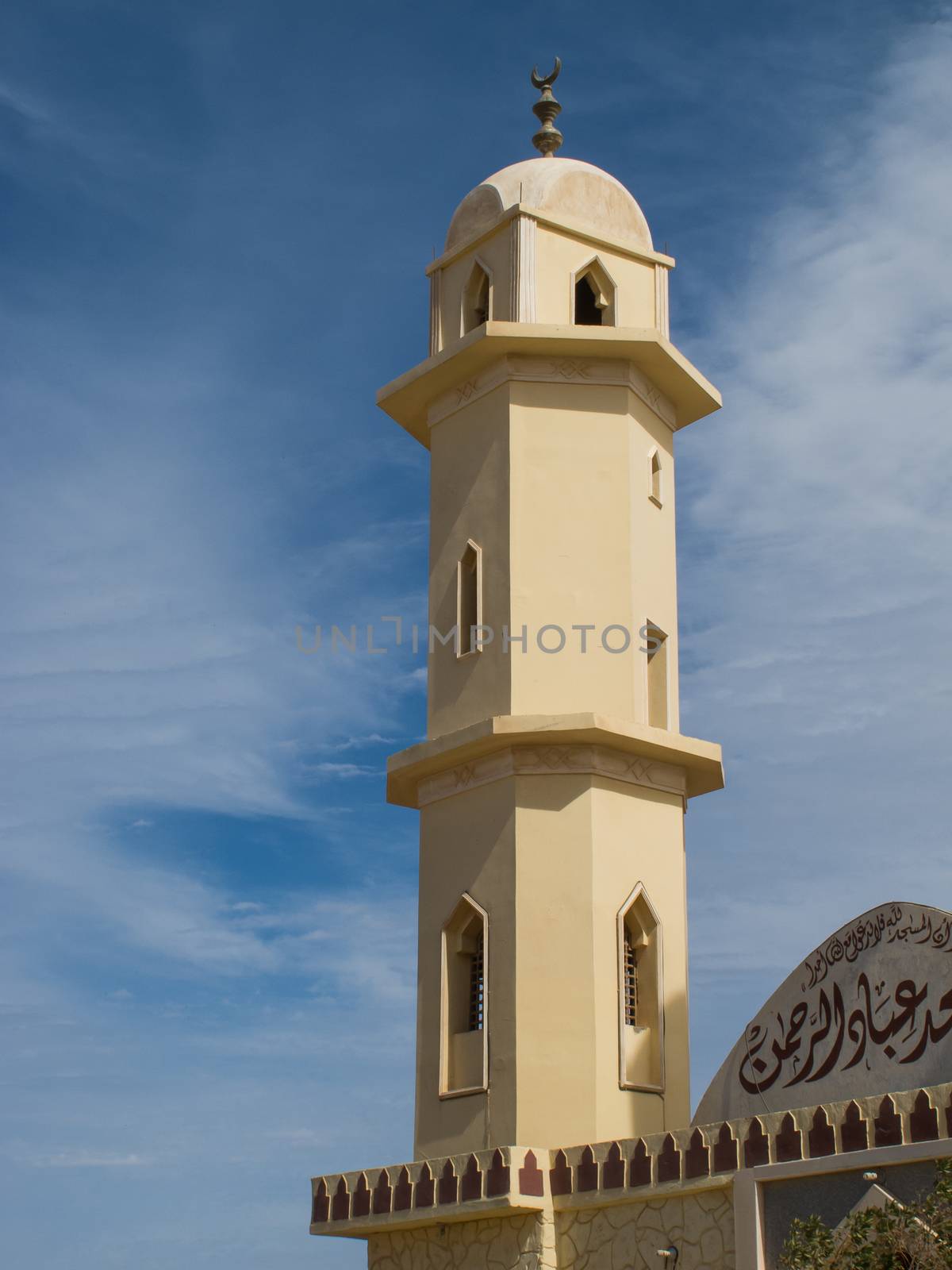 Light yellow color of the facade of a mosque in Egypt. Details of the tower. Blue sky with intense white clouds.