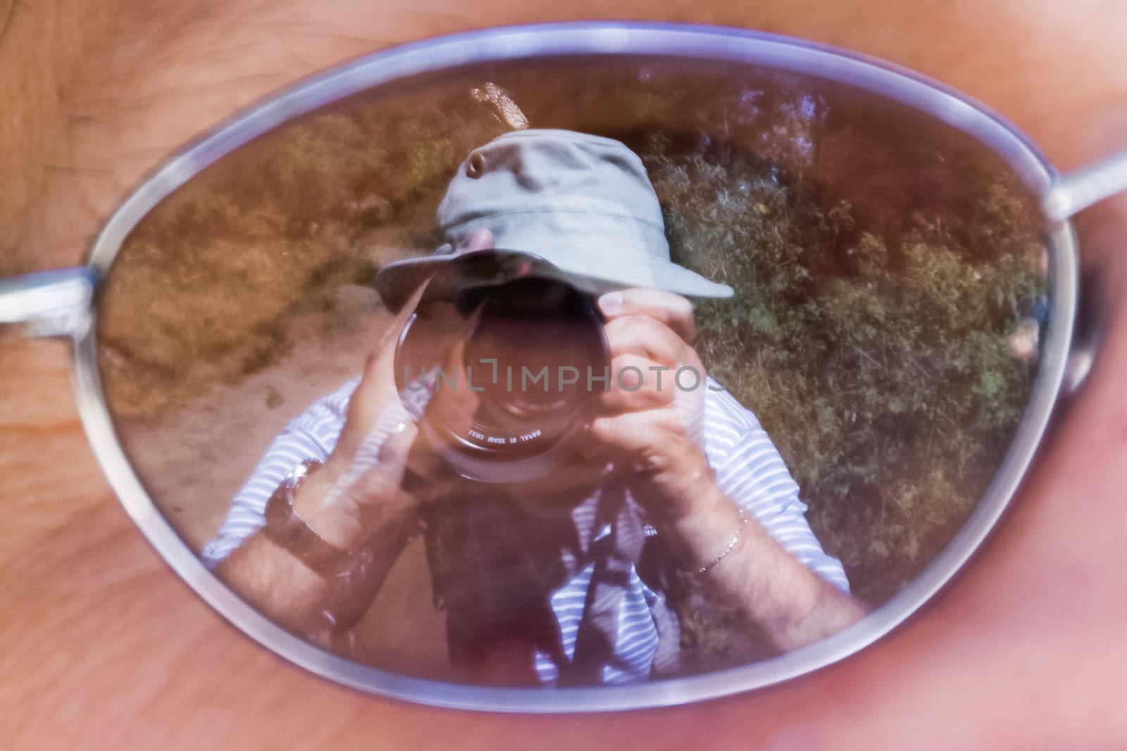 Mirror image of a photographer taking a picture of a Monarch butterfly on his own hat, using the reflection in the lens a woman's glasses