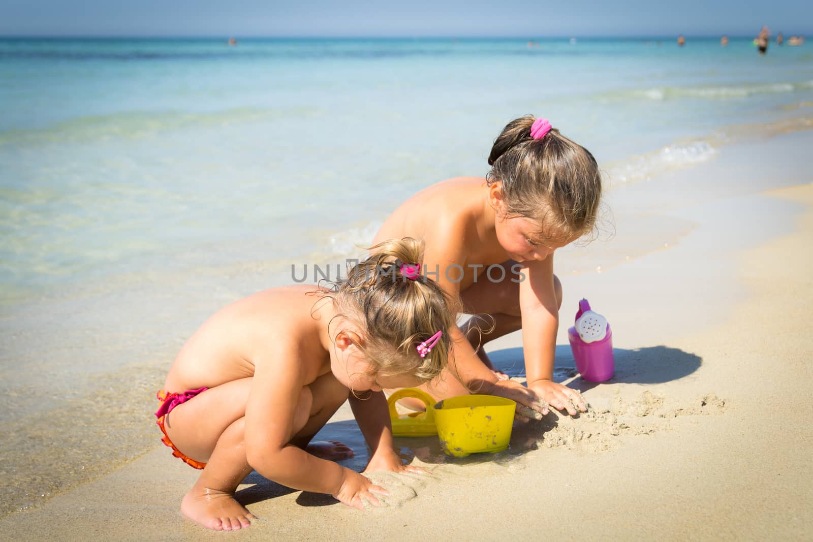 Two little girls playing with sand on the seashore.