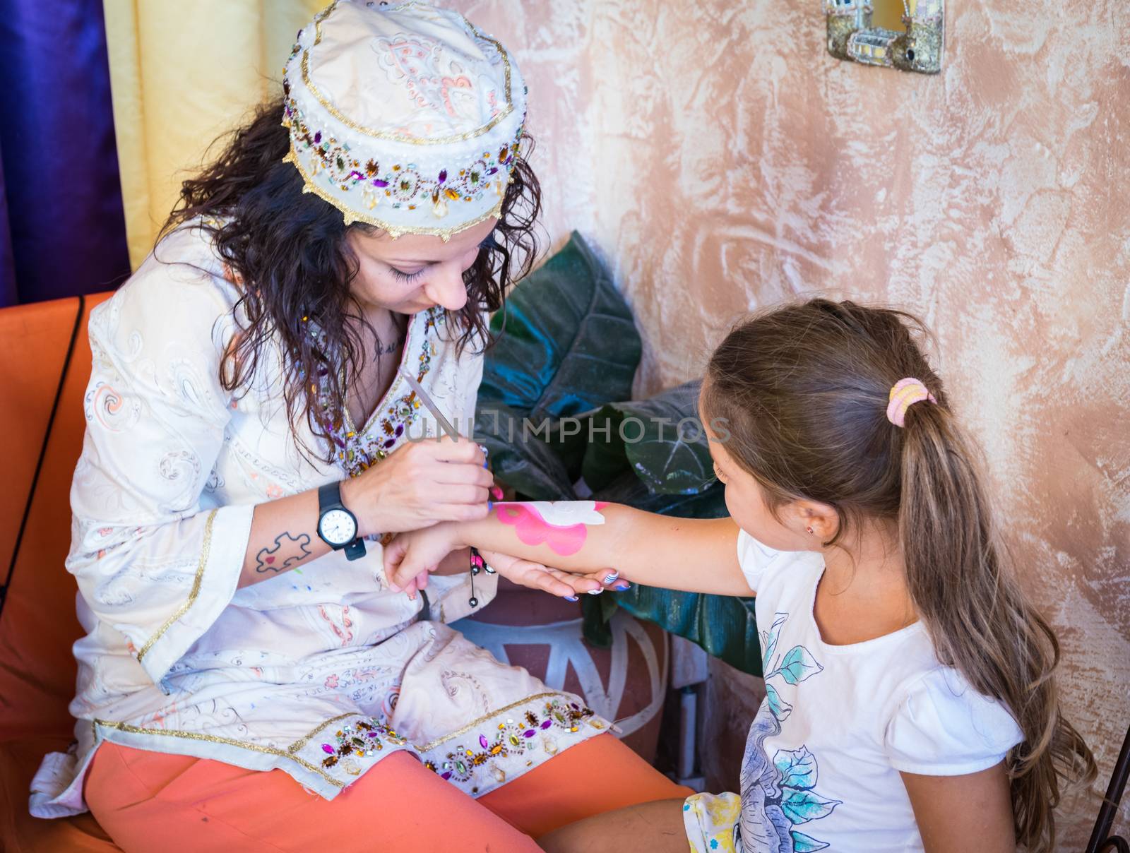 Girl paints a washable tattoo on the arm of a child. by Isaac74