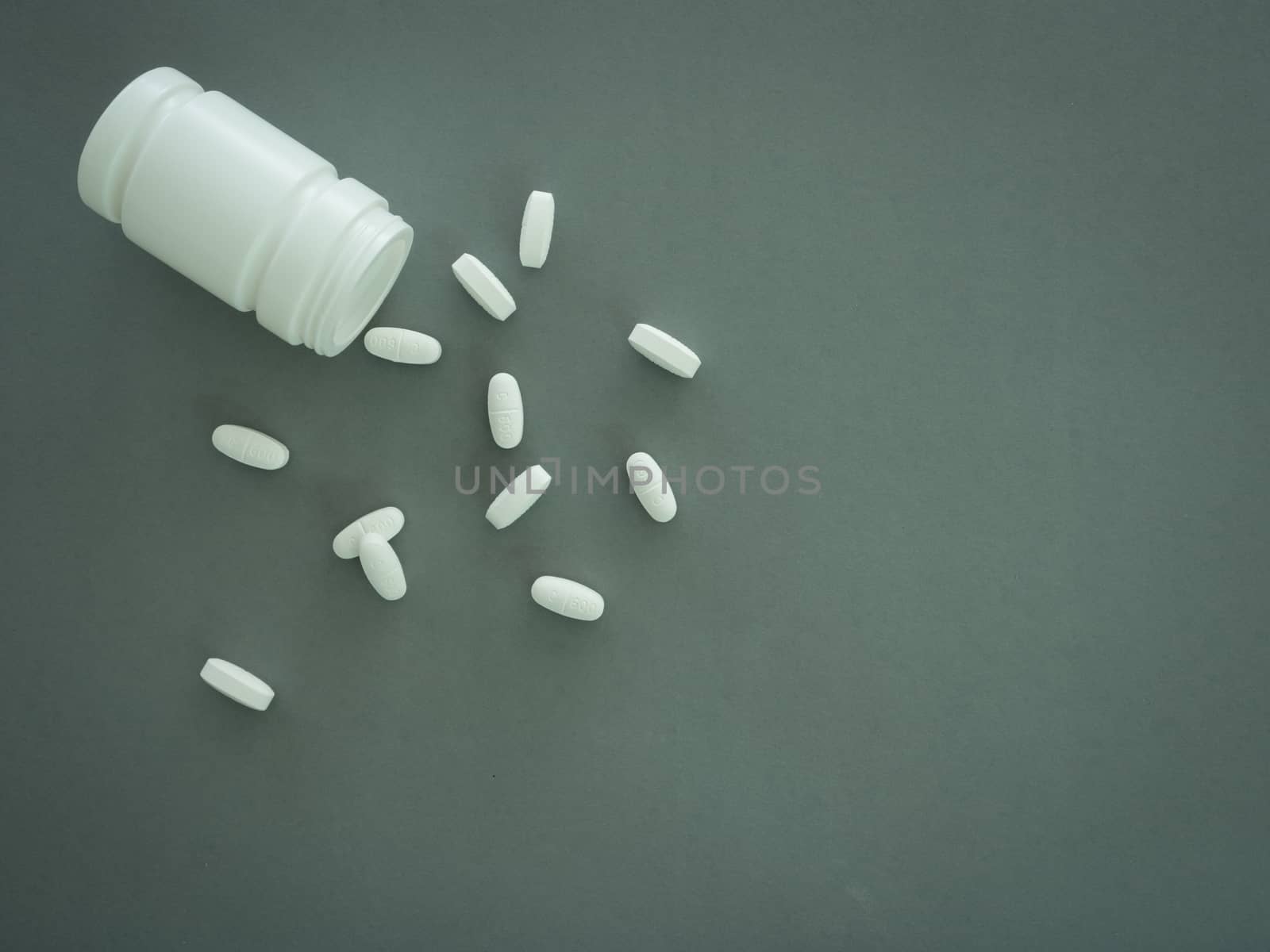 Pills spilling out of pill bottle on gray background. Top view