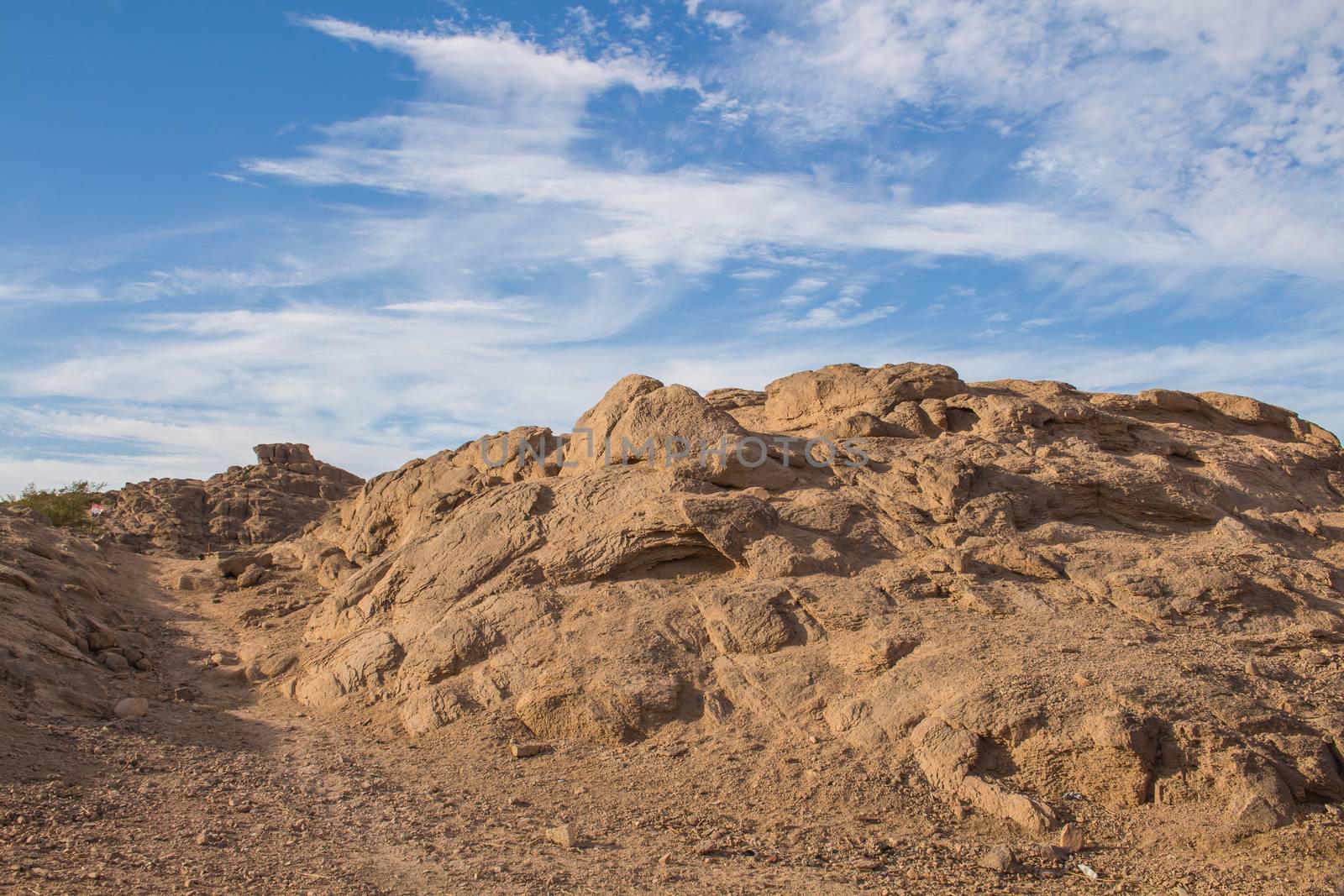 Detail of a rocky mountain in the desert in Egypt. Dark sand color, in some parts of the day looking like red. Contrast cloudy sky in the background.