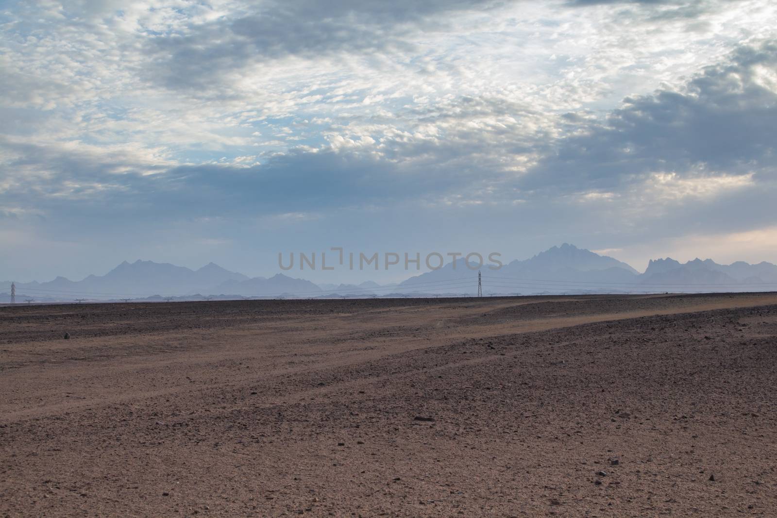 Plane sandy terrain in the desert in Egypt, close to the coast and city Hurghada. Line of mountains in the background. Intense clouds before the sunset.