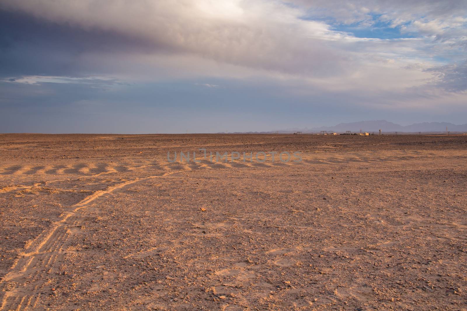 Plane sandy terrain in the desert in Egypt, close to the coast and city Hurghada. Line of mountains in the background. Intense clouds before the sunset.