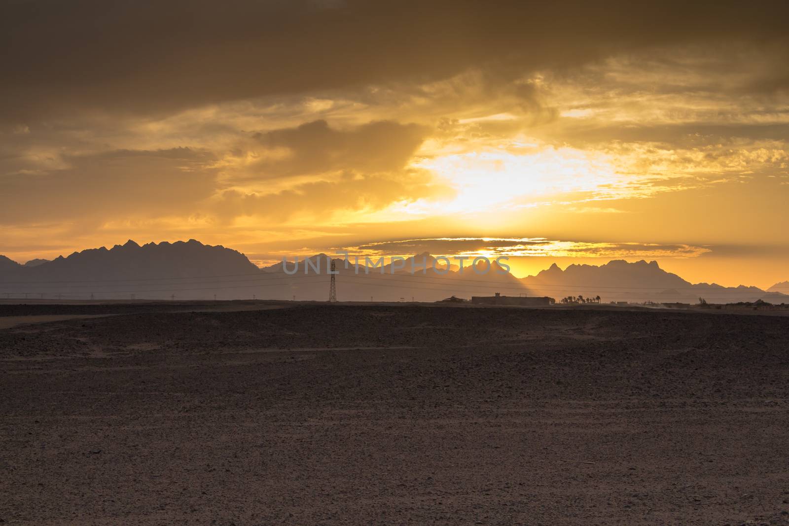 Sandy land in the foreground, rocky mountains in the background. Little clouds on the sky during the sunset.