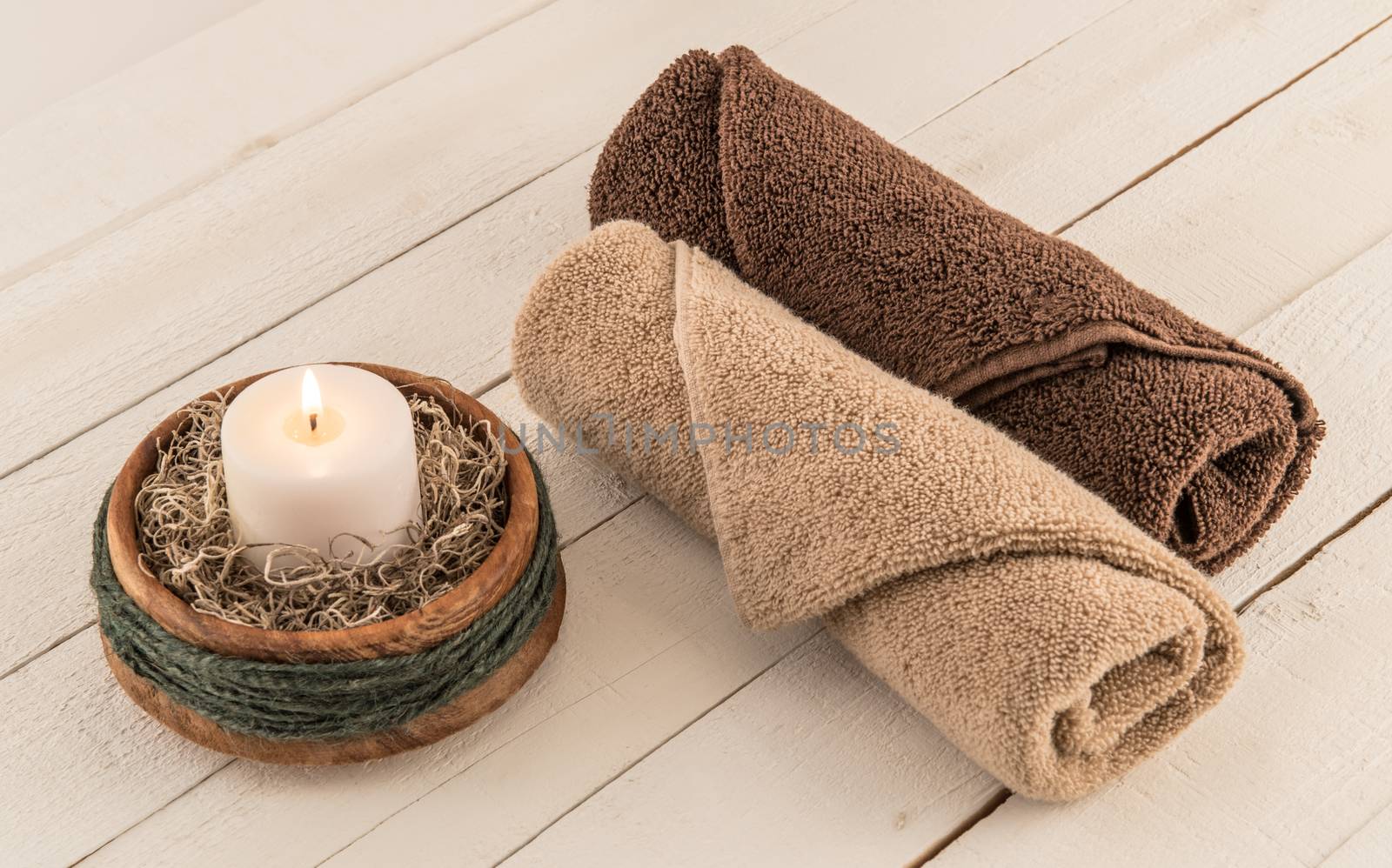 Beige and brown spa towels with aromatherapy candle, on rustic white plank background