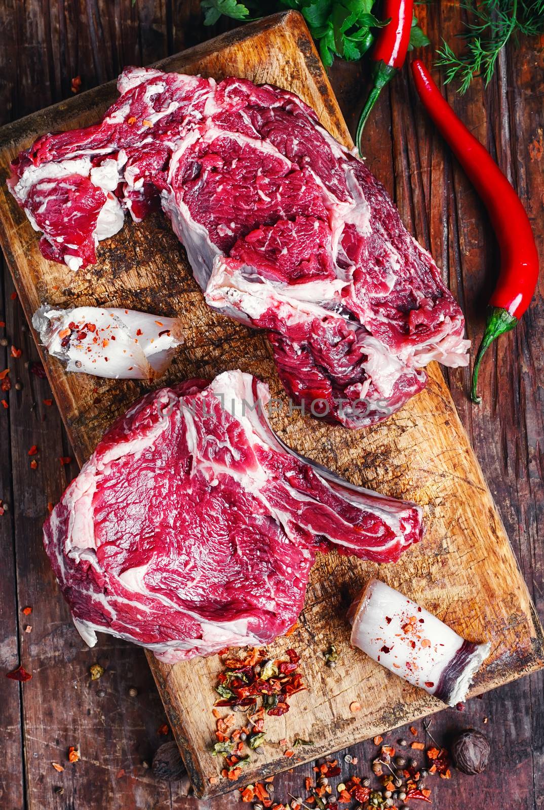 Chopped pieces of raw beef with spices on wooden cutting board