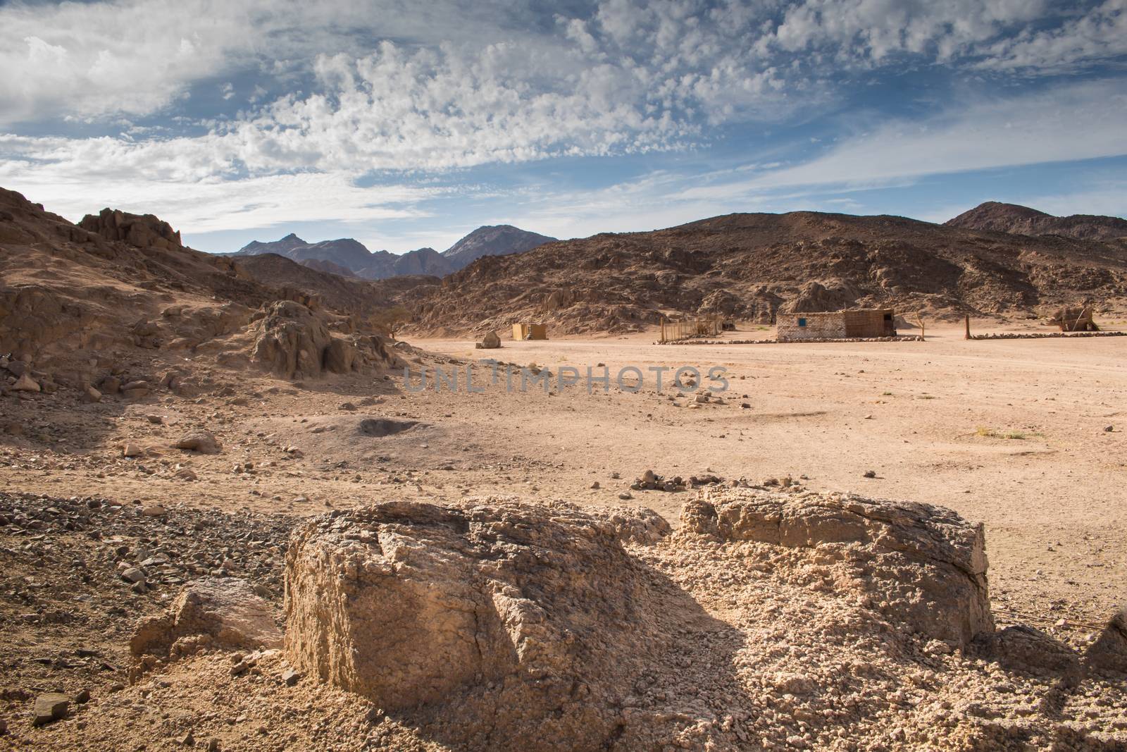 Valley between the rocky mountains in egyptian desert. Place of bedouin village, building visible. Intense cloudy sky.