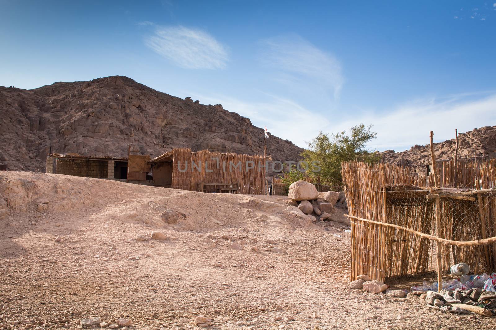 Bedouin village in the desert in Egypt, their buildings and fence. Rocky mountain in the background. Intense cloudy sky.