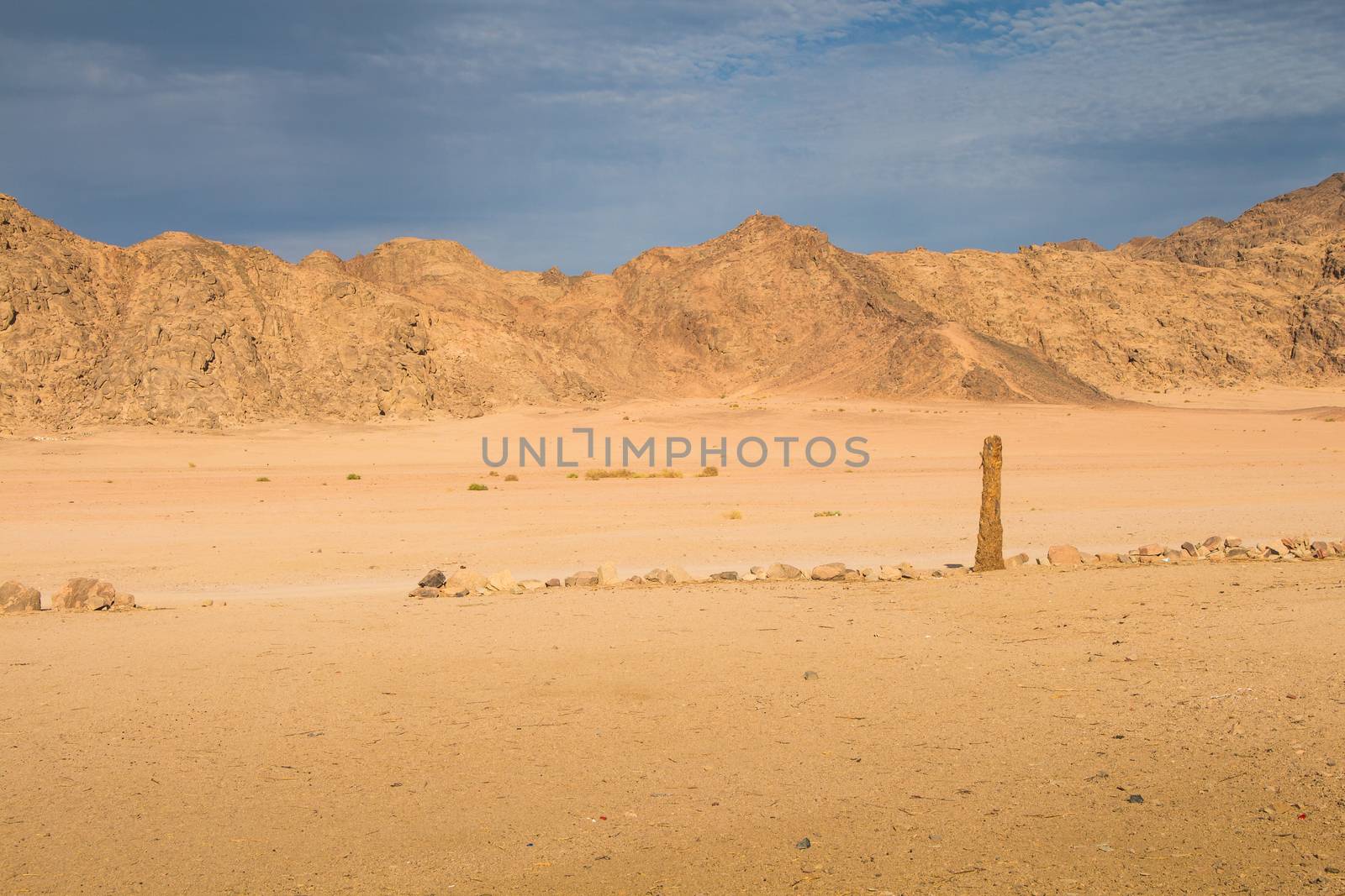 Valley between the rocky mountains in egyptian desert. Golden color of the sand and rocks thanks to the late afternoon sunlight. Cloudy sky.