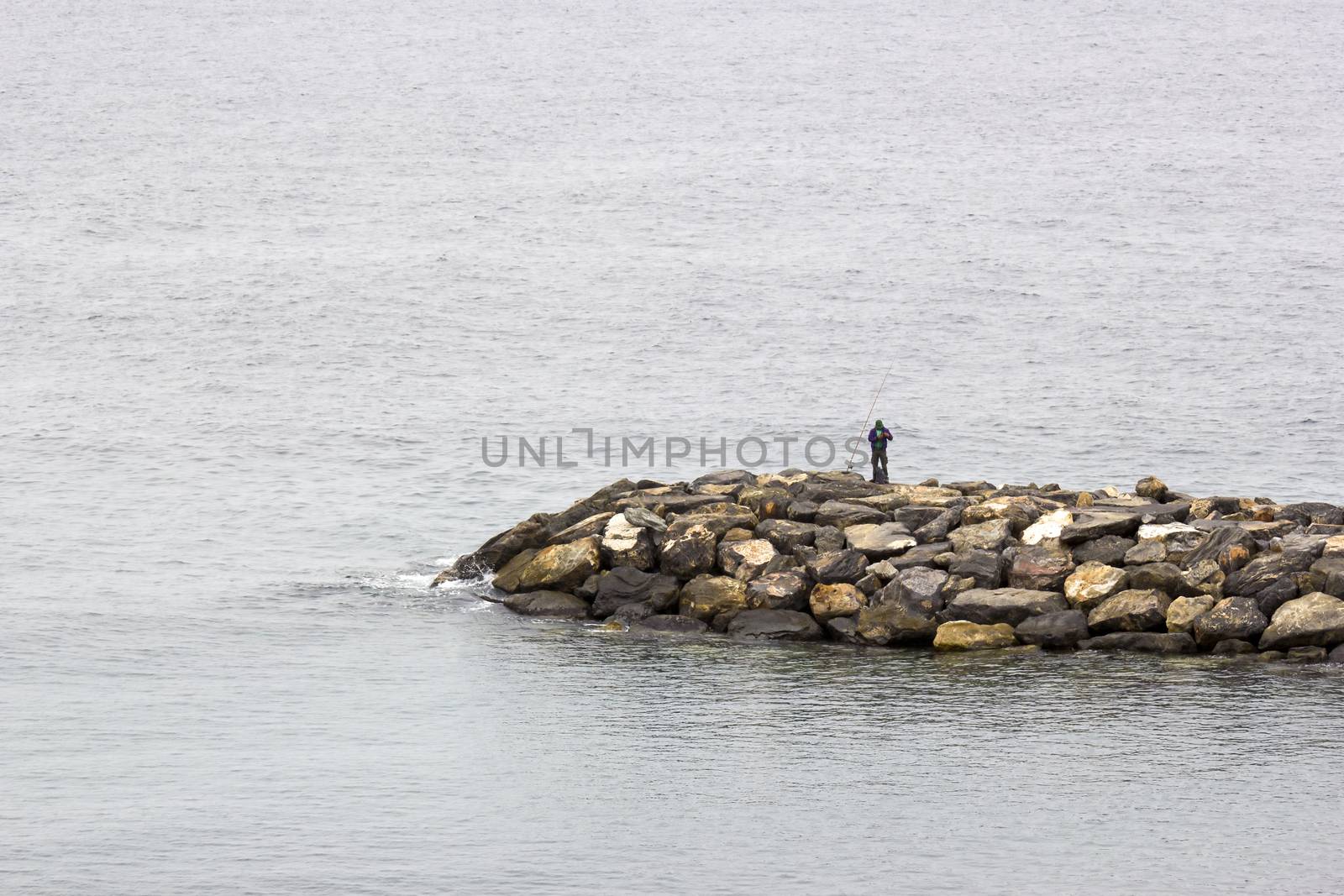Fisher man with fishing rod on the stone groyne