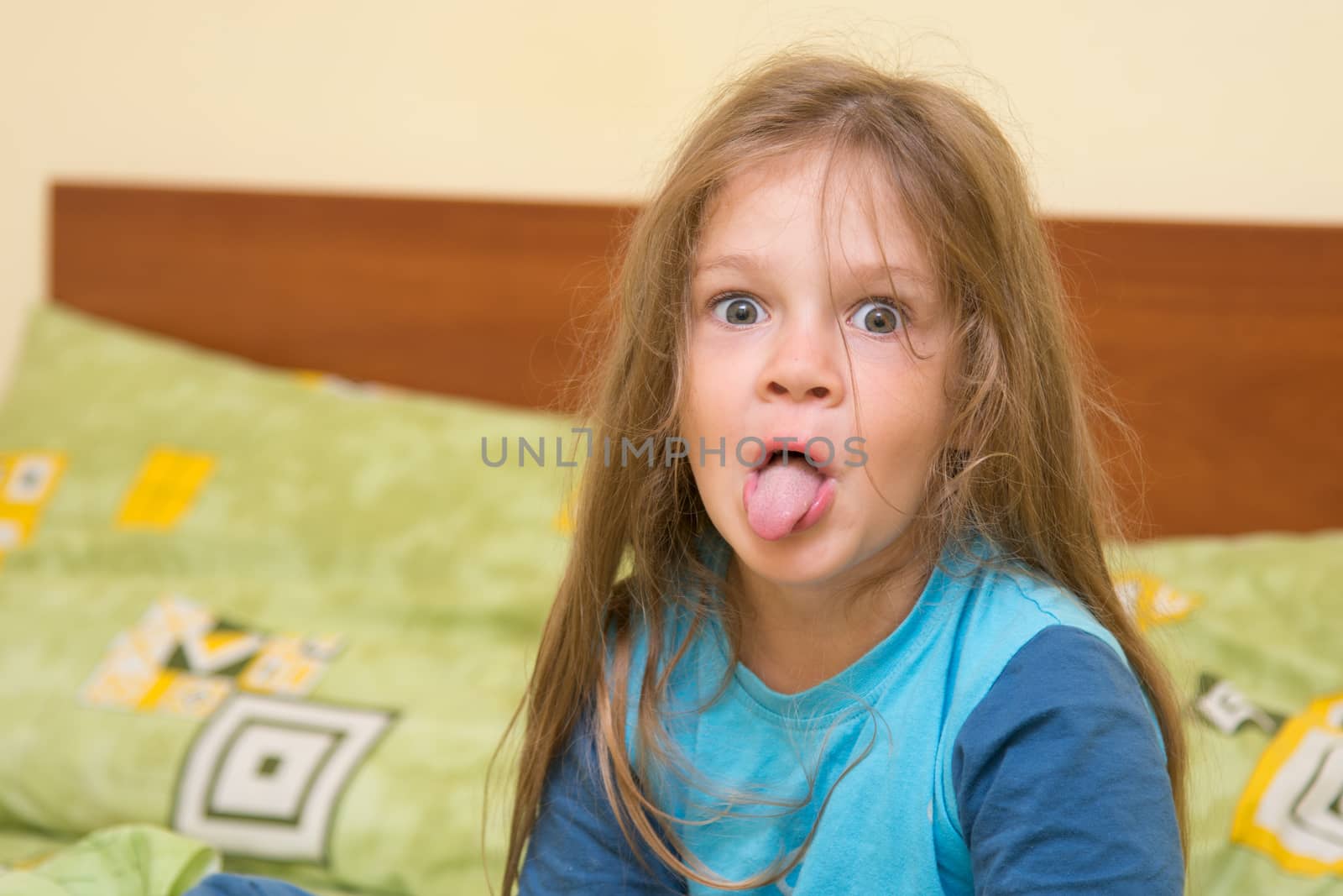 Funny five-year girl waking up sitting on the bed in pajamas