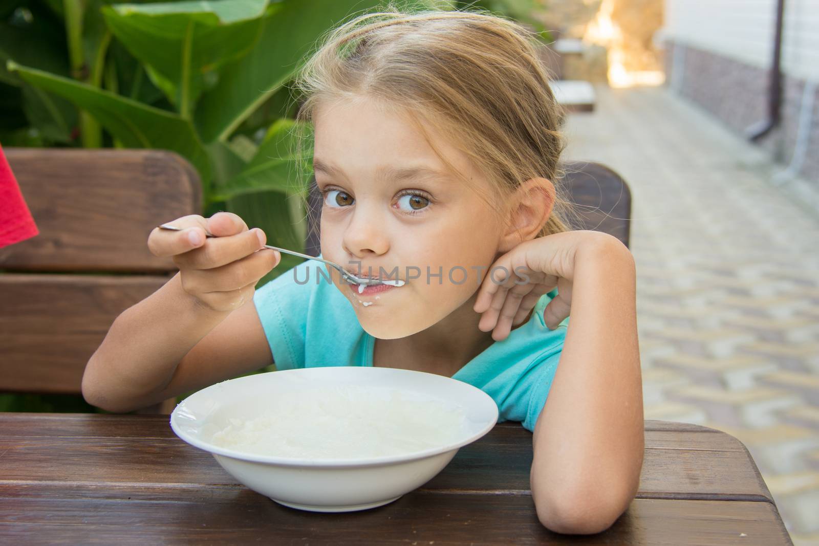 Six-year girl sitting at a table on the veranda and enjoy eating porridge