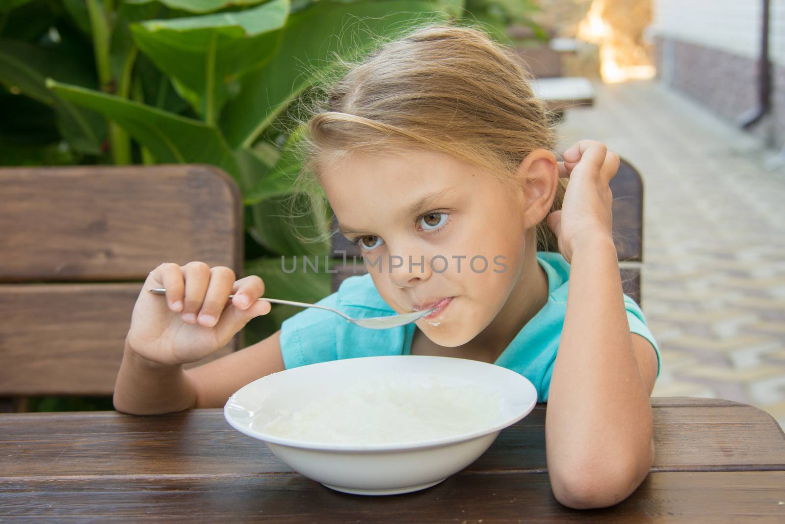 Six-year girl sitting at a table with a sour face and did not want to eat porridge for breakfast
