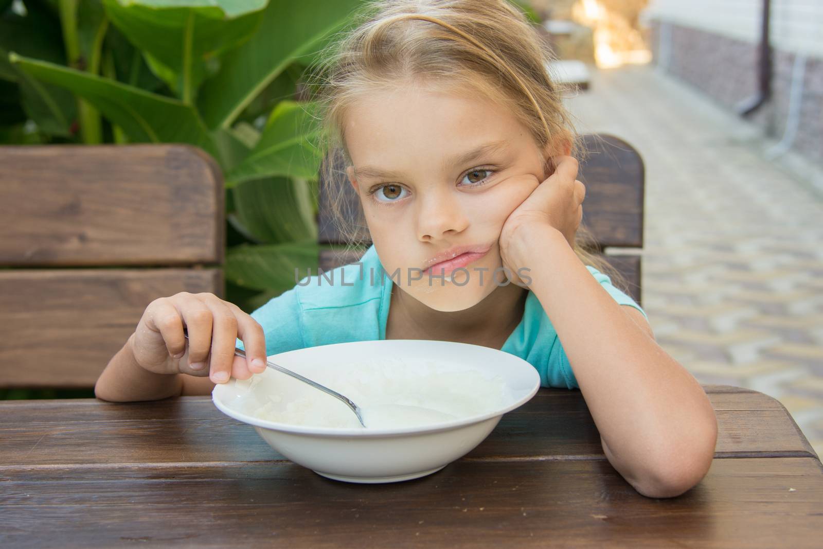 Six-year girl sitting at a table with a sour face and did not want to eat porridge for breakfast