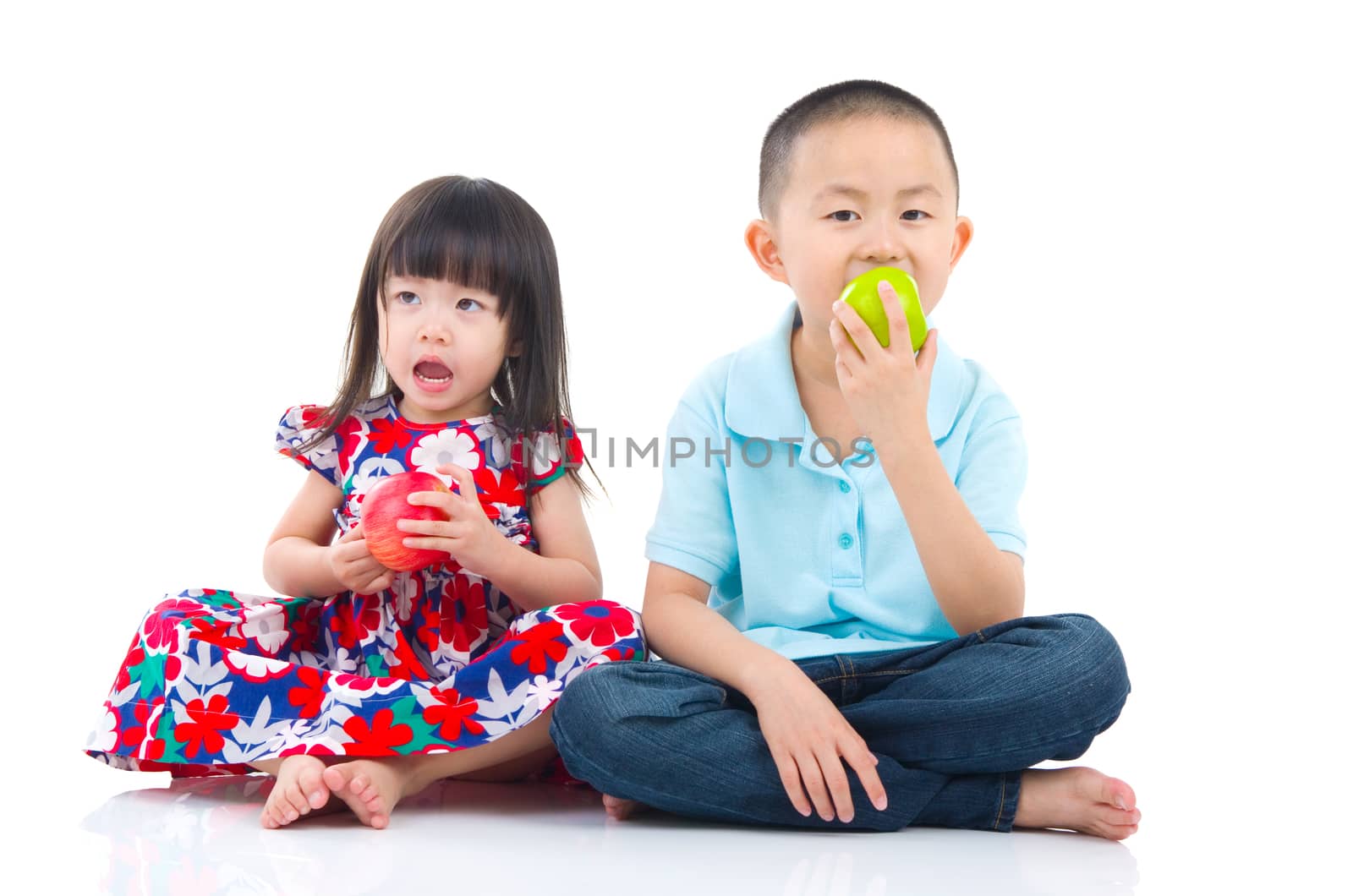 Asian brother and sister sitting on the floor and eating an apple