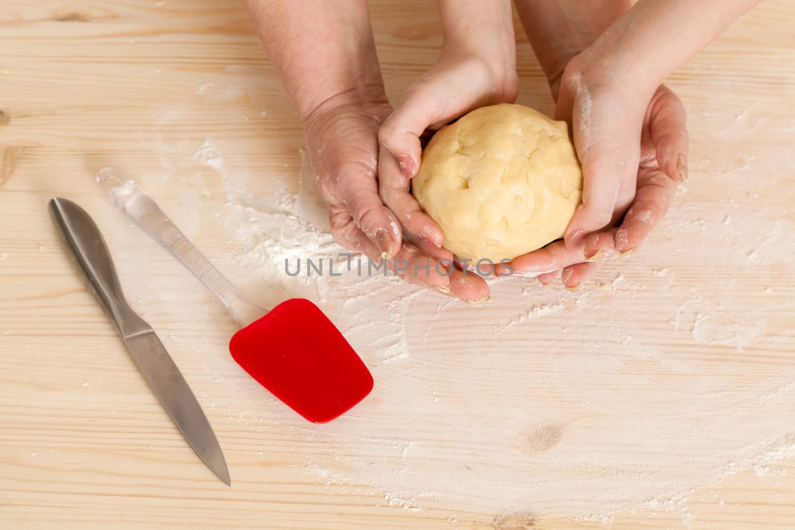 hands of the grandmother and hand of the granddaughter hold dough on a kitchen table