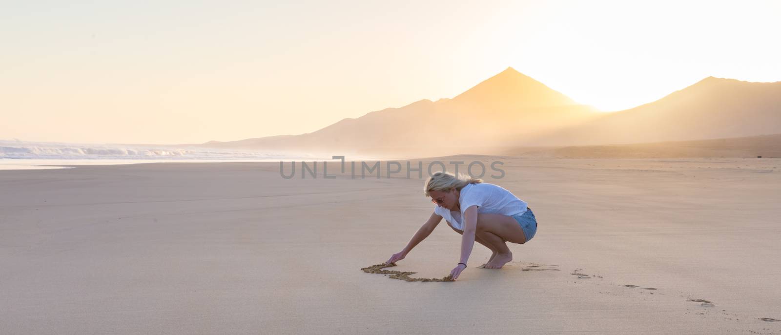 Lady drawing heart shape in sand on beach. by kasto