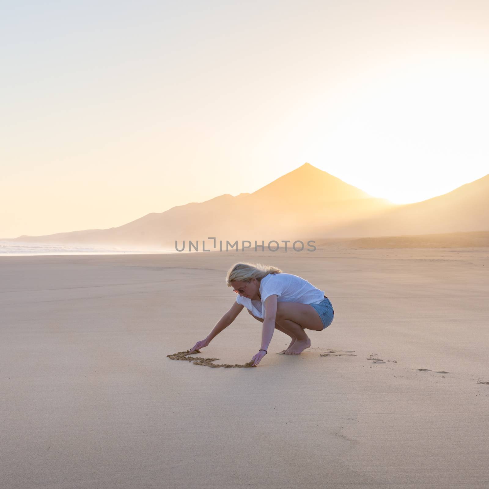 Lady drawing heart shape in sand on beach. by kasto