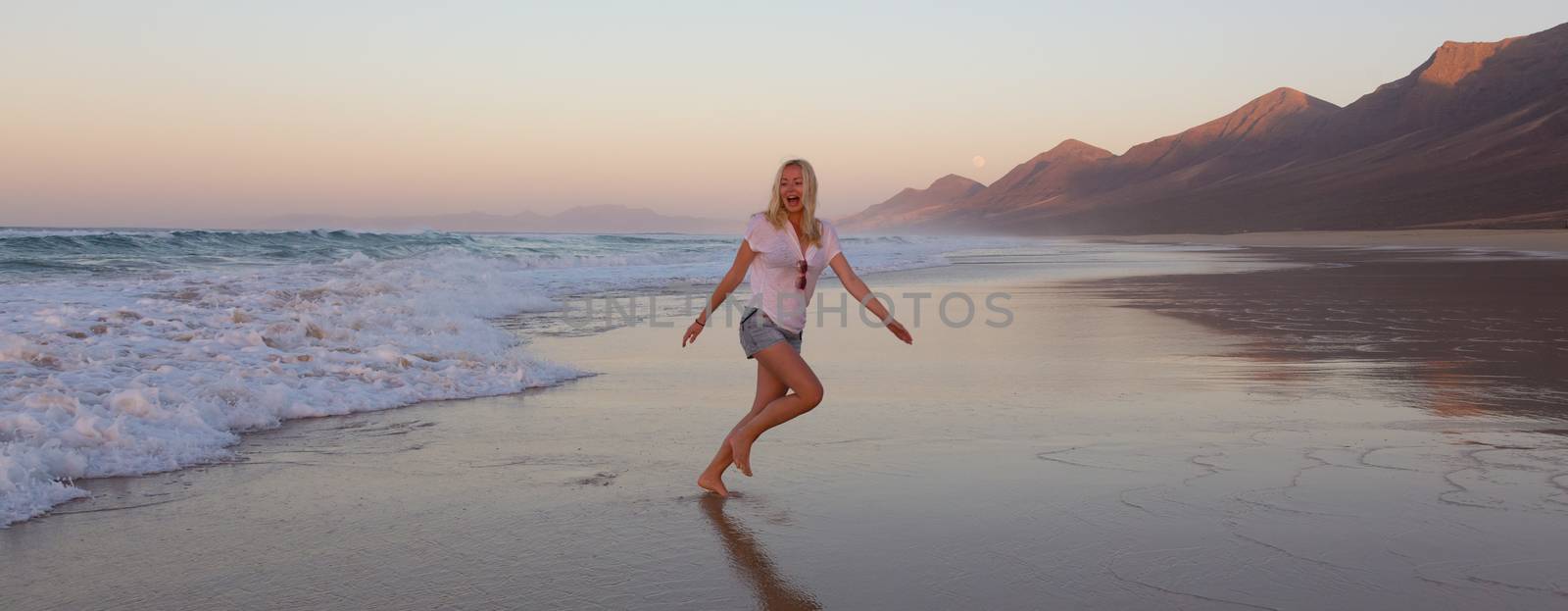 Lady enjoying running from waves on sandy beach in sunset. by kasto