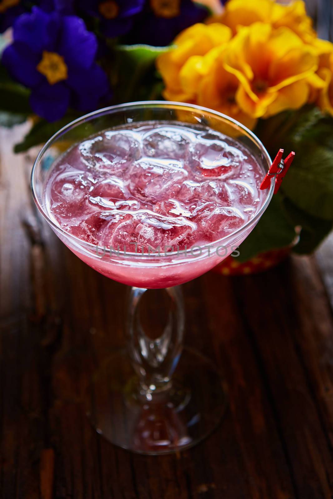 cosmopolitan cocktail garnished with ice on wooden table and flowers background