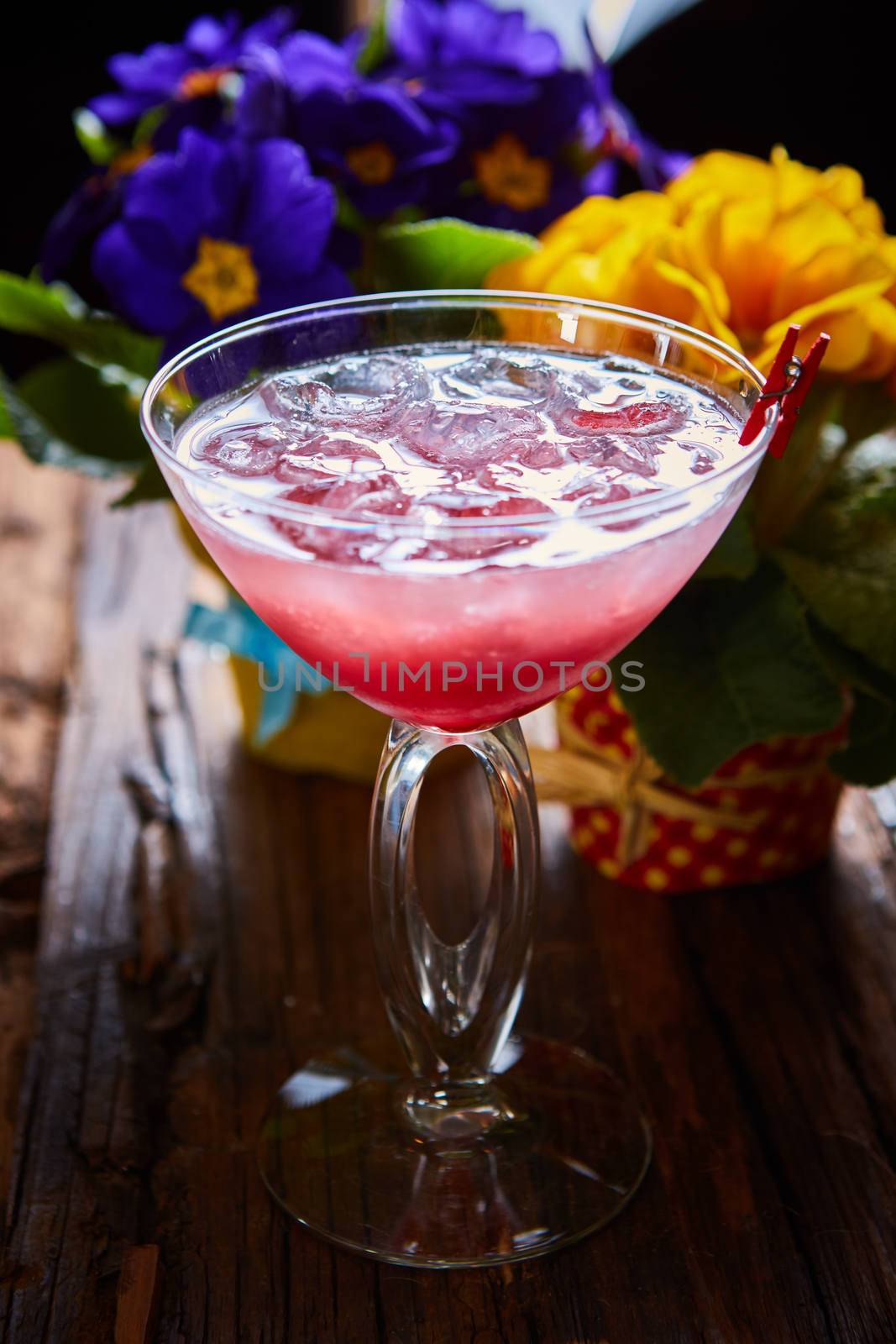 cosmopolitan cocktail garnished with ice on wooden table and flowers background