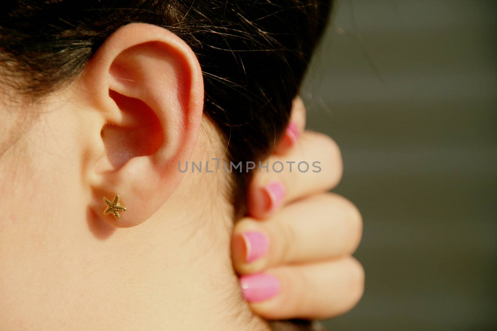 side view of female person holding hair to side with pink nail polished fingers showing starfish earing on ear