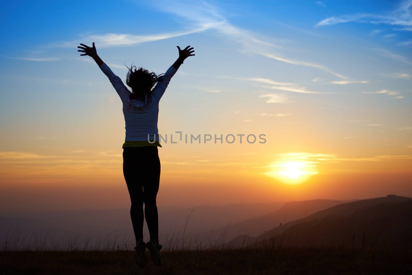 Silhouette of young woman jumping against sunset