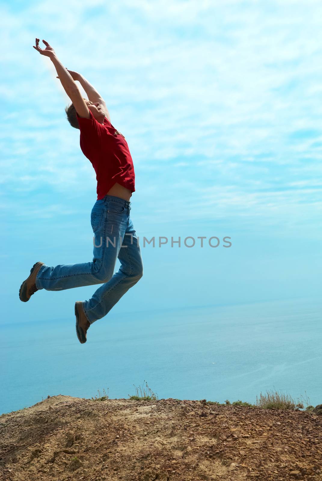 Man jumping cliff against sea and mountain with blue sky