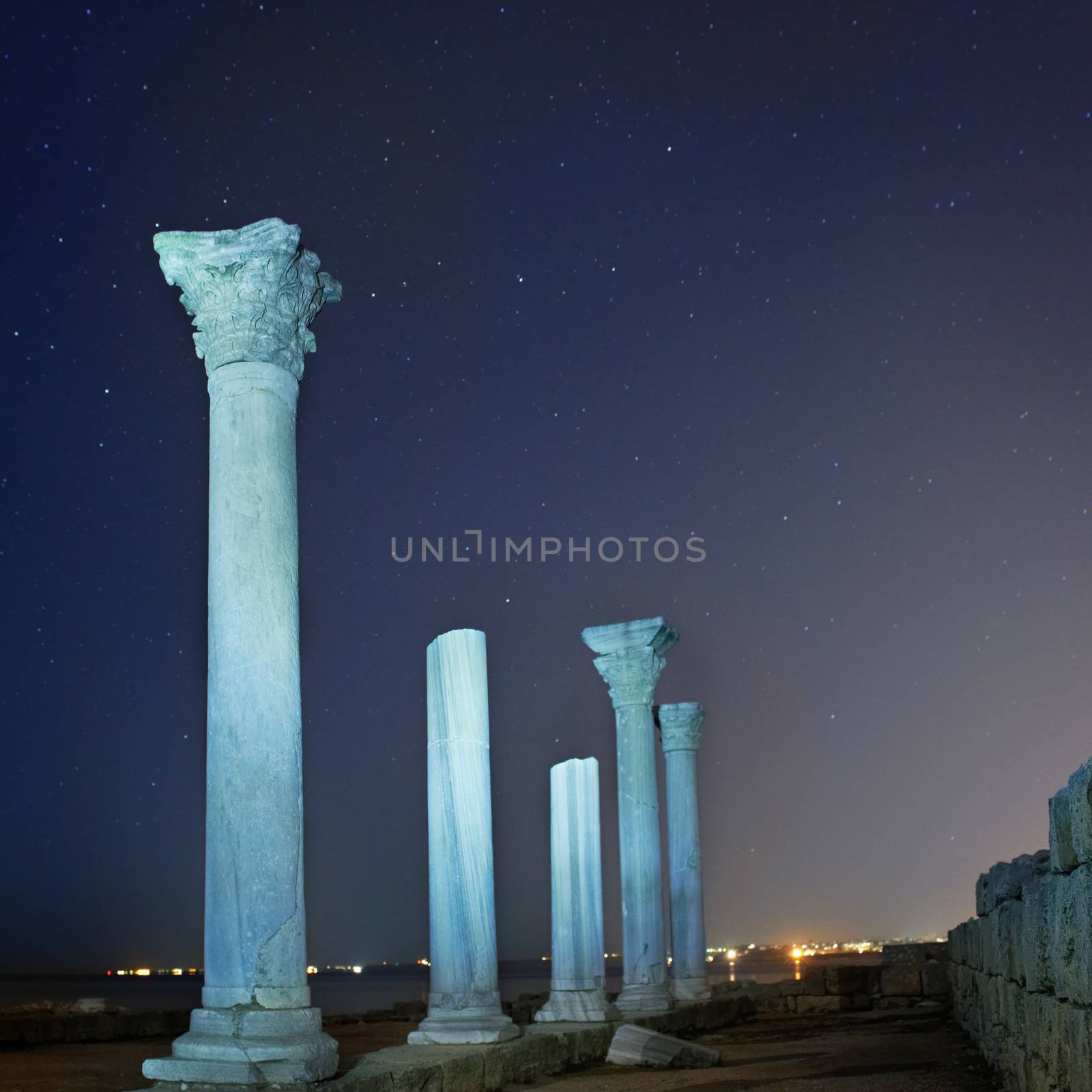 Ruins of ancient city columns under blue night sky with moon and stars