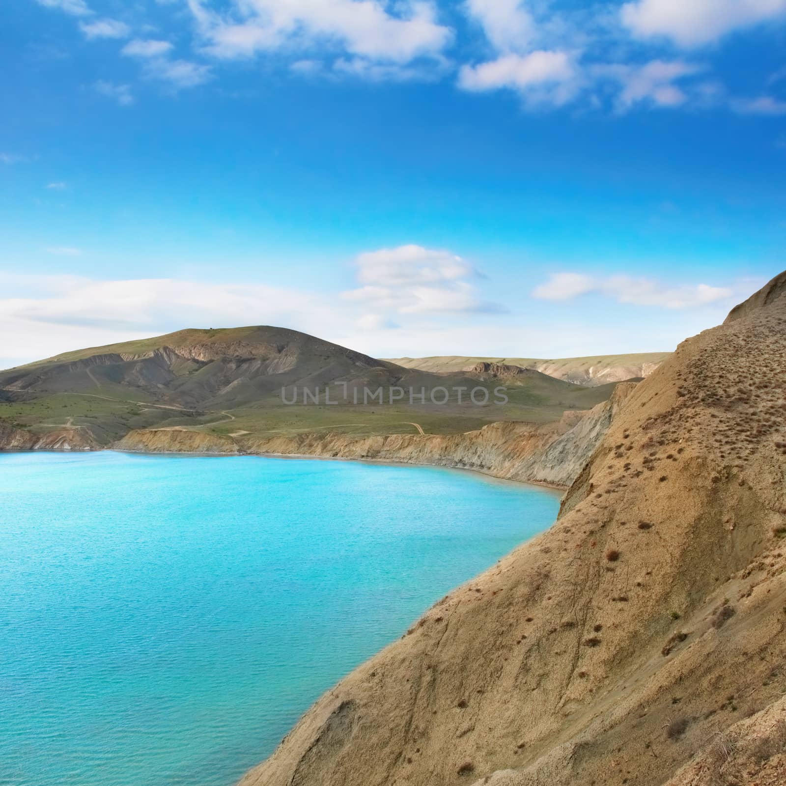 Sea harbor with blue water, green field and blue sky with clouds