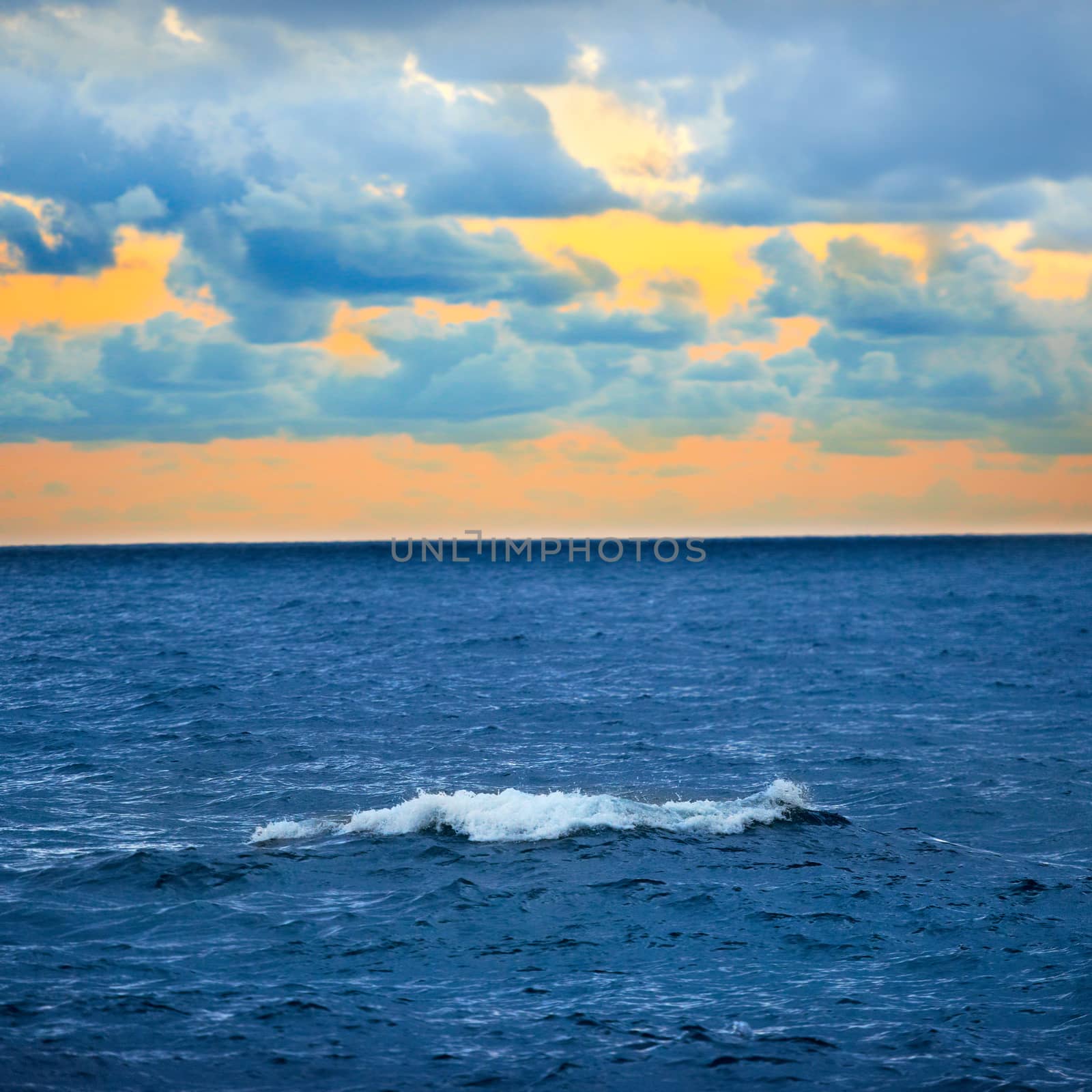 Big wave, colorful sunset over the sea with blue sky and clouds