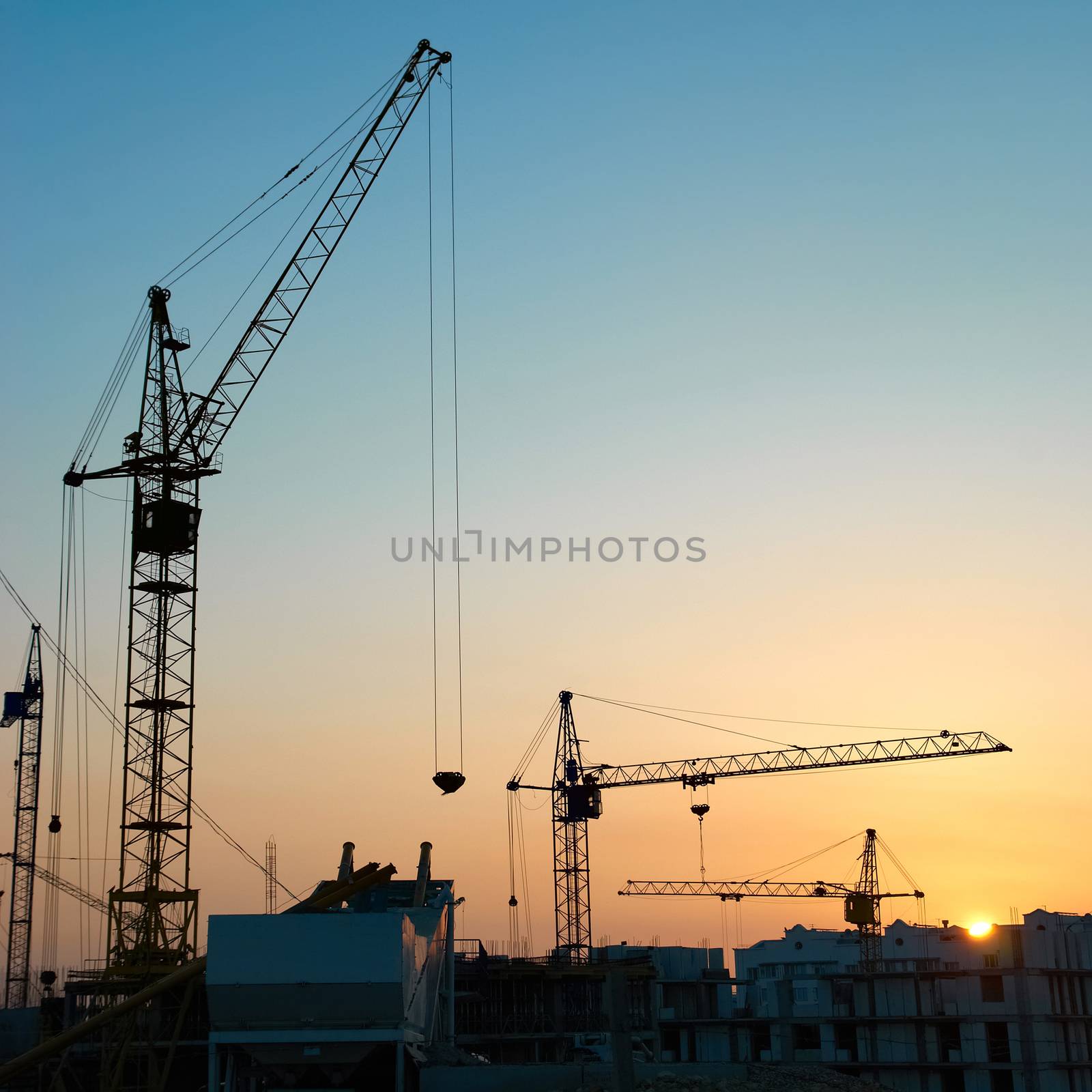 Industrial landscape with silhouettes of cranes on the sunset background