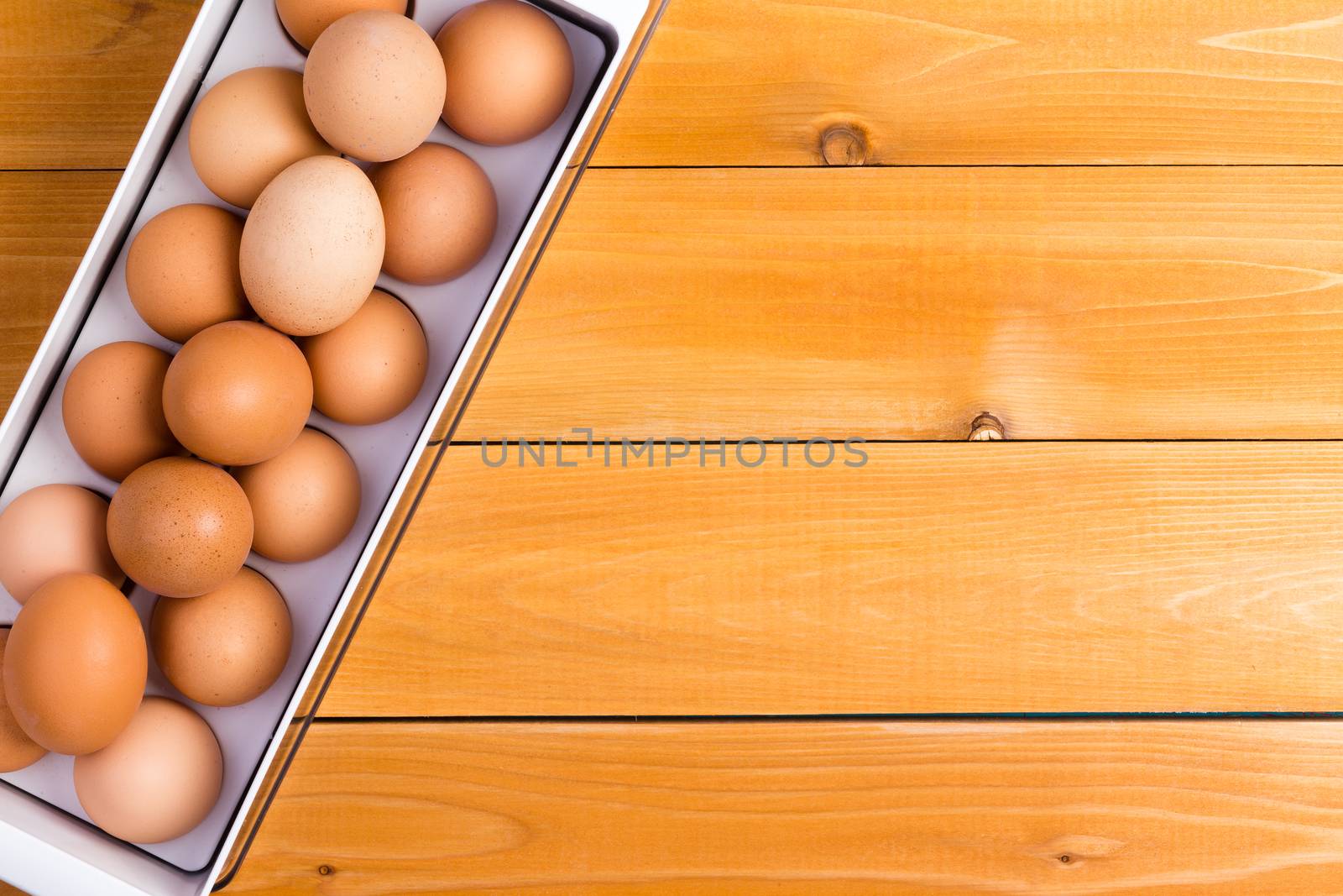 Storage container of healthy brown farm eggs on a wooden table with copy space viewed from above