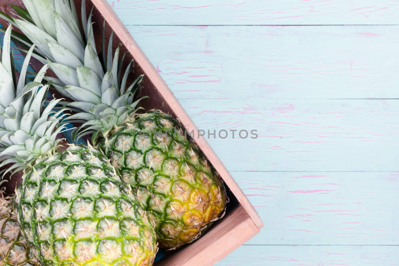 Fresh pineapples in a wooden crate displayed at an angle on a blue painted wooden table with copy space, overhead view