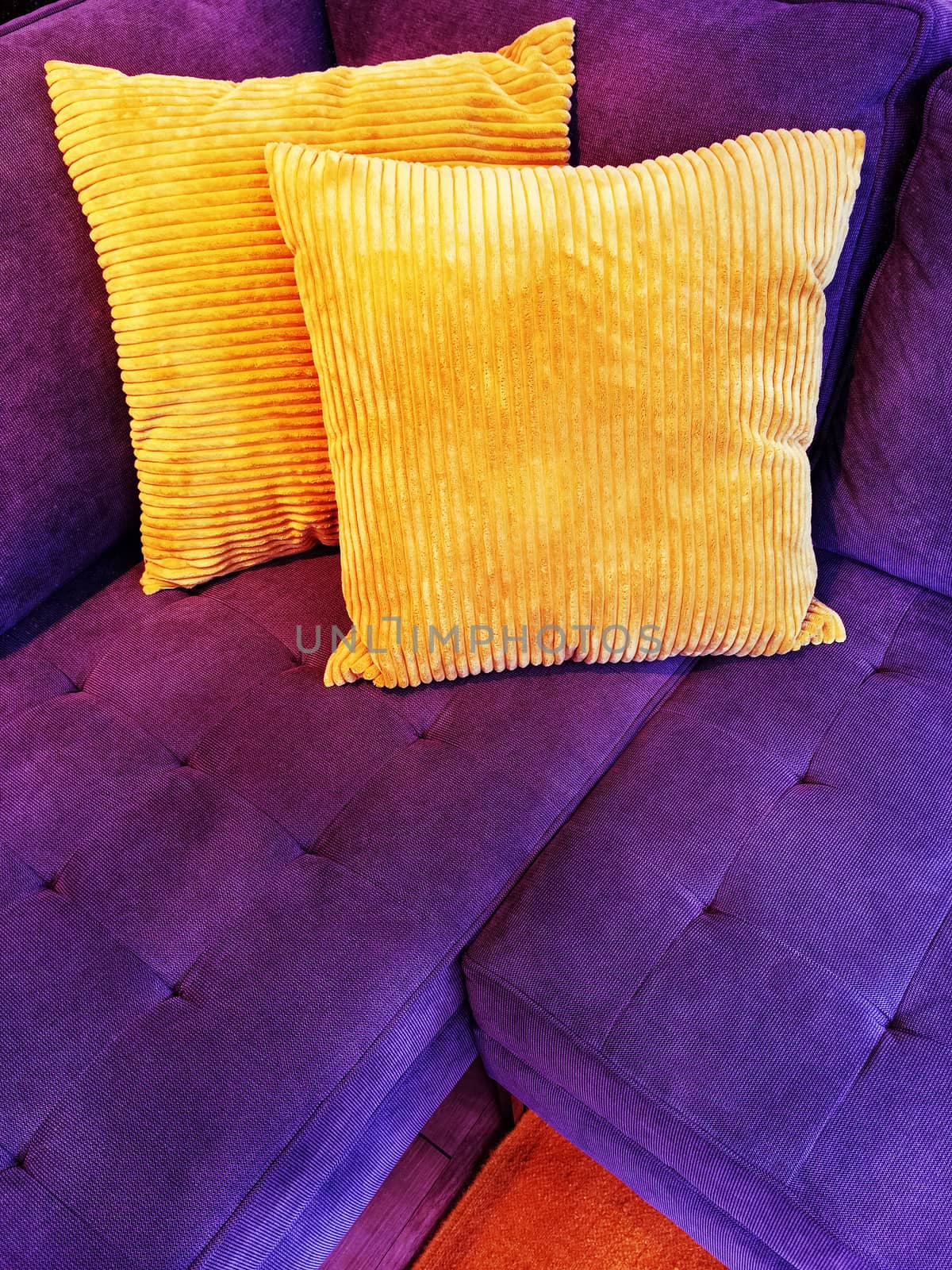 Vibrant purple sofa decorated with two orange cushions.